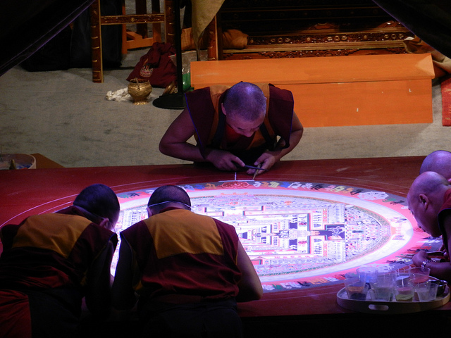 Tibetan Buddhist artist monks completing the lettering around the Kalachakra mandala, one fills in the white edge, others wear masks, plastic cups of colored sand, on stage, Kalachakra for World Peace, Washington D.C., USA